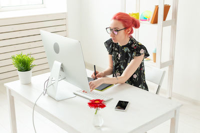 Young woman using phone while sitting on table at home