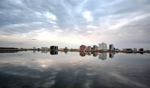 City at waterfront against cloudy sky