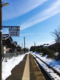 Railroad tracks by road against sky during winter