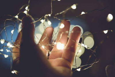 Cropped hand holding illuminated string lights at night