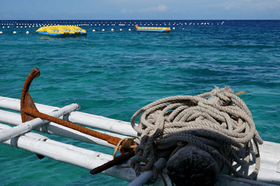 Rusty anchor and rope on bamboos over sea by inflatable rafts against sky