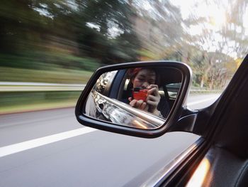 Reflection on woman clicking selfie on side-view mirror