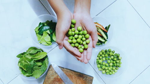 Cropped hands holding green peas in kitchen