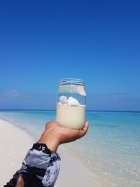 Man holding glass of water at beach against blue sky