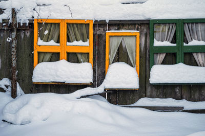 Snow-covered colorful window frames by a wooden fence, decorations in the childrens playground