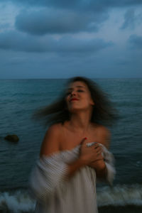 Barefoot female traveler in light dress walking among small sea waves on empty coastline at dusk