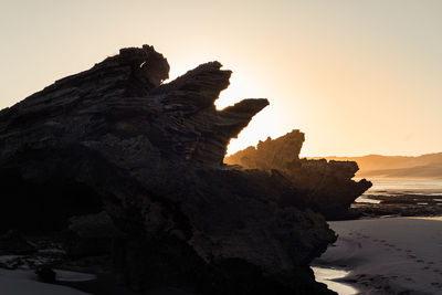 Rock formation on shore against sky during sunset