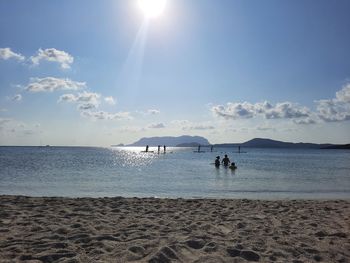 People on beach against sky during sunny day