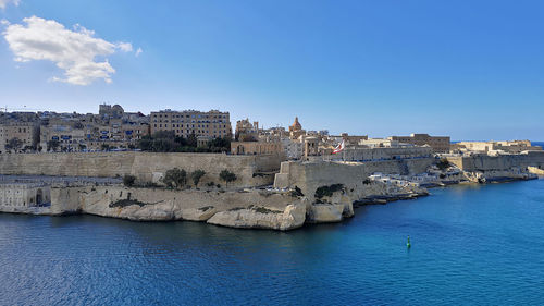 Buildings by sea against blue sky