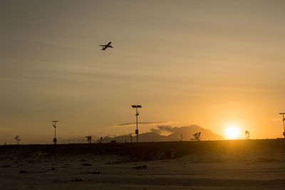 Silhouette airplane flying over land against sky during sunset