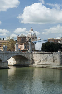 Arch bridge over river by buildings against sky in city