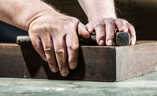 Cropped hands of man holding work tools on table in workshop