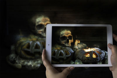 Cropped hands of person photographing spooky halloween decorations with digital tablet