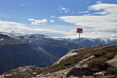 Information sign on mountain against cloudy sky during sunny day