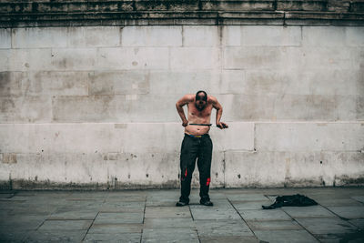 Full length of shirtless man standing against wall