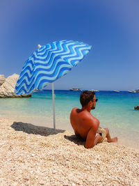 Shirtless man looking away while relaxing at beach
