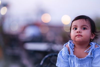 Cute baby girl looking away in city at sunset