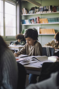 Boy studying while sitting on desk in classroom