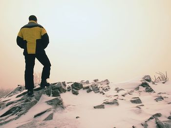 Rear view of man standing on snowcapped mountain against sky