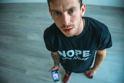 High angle portrait of young man holding mobile phone on hardwood floor