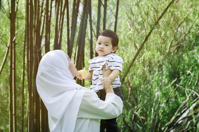 Side view of mother playing with son against trees