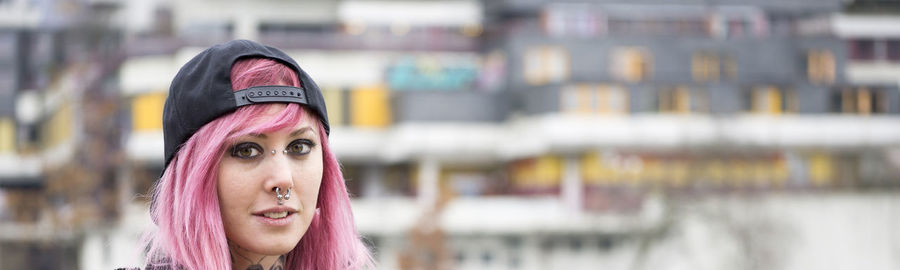 Young alternative woman with piercings and pink hair in front of defocused housing estate 