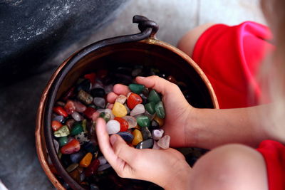Midsection of boy holding colorful stones over bucket