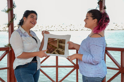 Happy friends holding mirror frame at gazebo