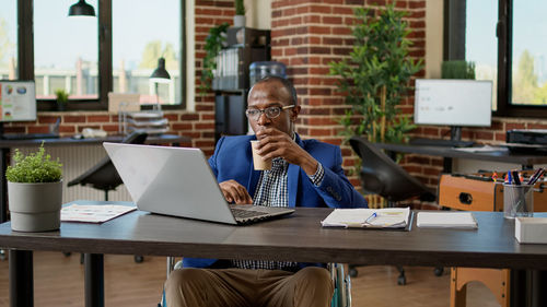 Businesswoman drinking coffee sitting with laptop on wheelchair in office