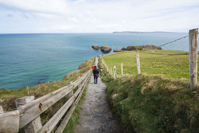 People on footpath by sea against sky