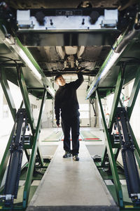 Full length of male mechanic examining car on hydraulic lift in auto repair shop