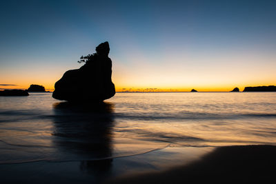 Silhouette rock on beach against sky during sunset