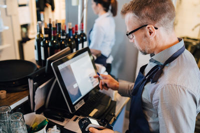 Owner using computer while holding credit card reader in restaurant