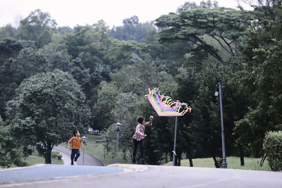 Boys flying kite while running on road by trees