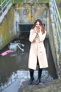 Woman covering face with scarf while standing near polluted water