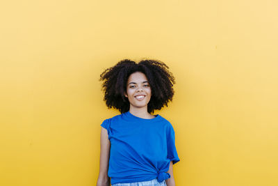 Pretty woman standing in front of yellow wall, smiling happily