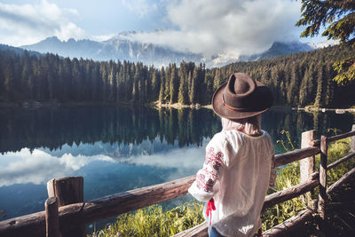 Rear view of woman looking at trees by lake against mountains