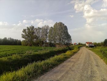 Dirt road amidst field against sky