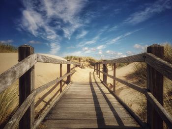 Boardwalk leading towards footbridge against sky