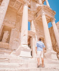 Rear view of man standing by old ruin during sunny day