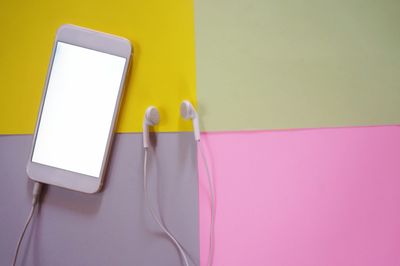 High angle view of mobile phone and headphones against multi colored background