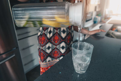 Cropped image of woman pouring lemonade in glass at table