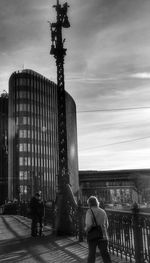 People walking in city against cloudy sky