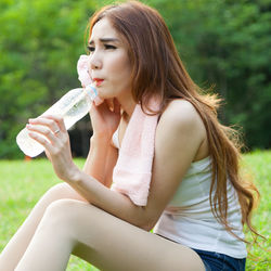 Woman drinking water from bottle while sitting on field