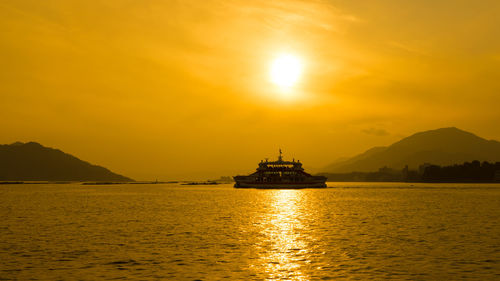 Silhouette ship in sea against orange sky