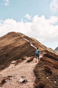 Rear view of man walking on mountain against sky