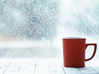 Close-up of coffee cup on table against glass window during winter