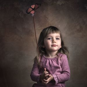 Portrait of cute girl holding butterfly against wall