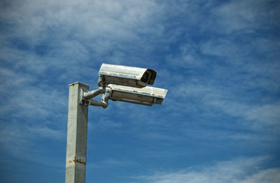 Low angle view of security cameras against blue sky