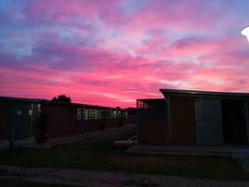 House on field by buildings against dramatic sky